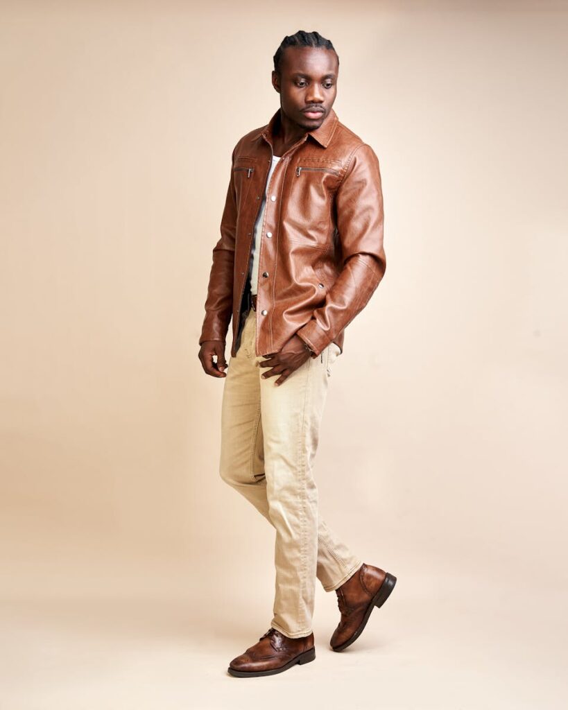 A fashionable man in a leather jacket posing in a studio setting.