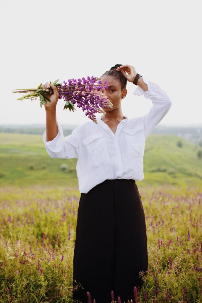 Portrait of a stylish woman holding purple lupines in a vibrant flower field.