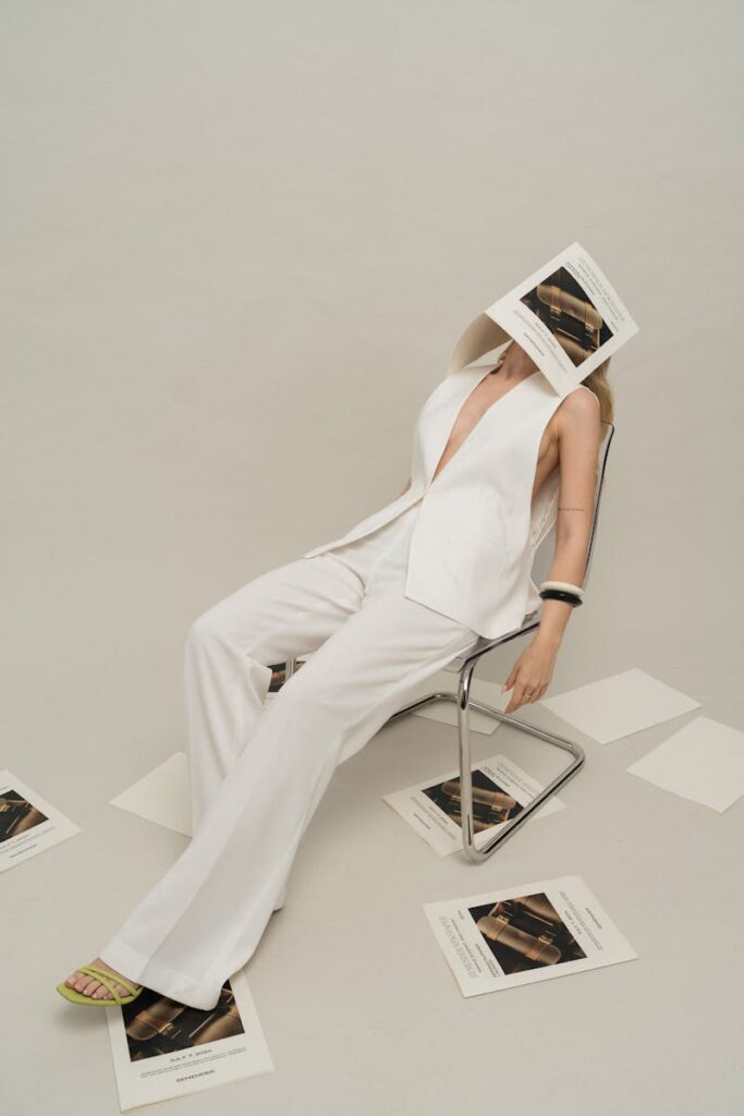 Fashionable woman in white attire poses in a studio with scattered papers.