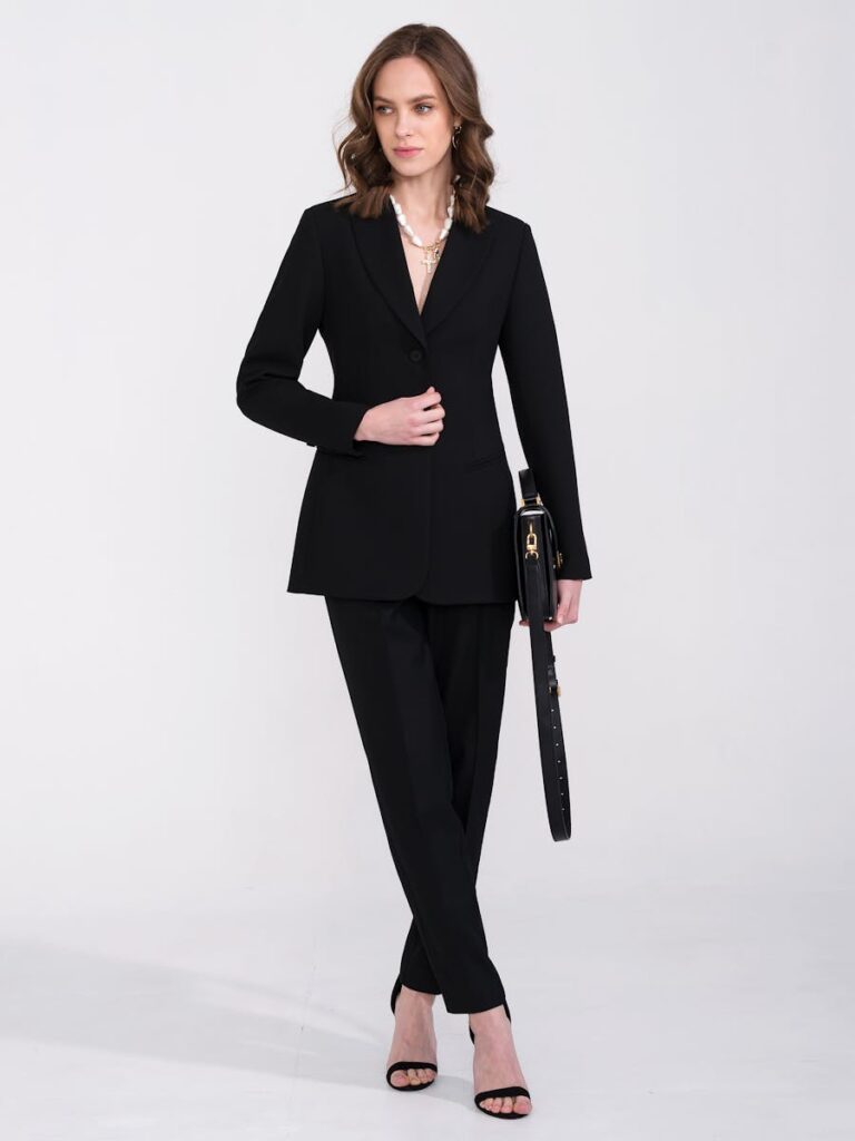 A stylish woman in a black suit poses elegantly in a studio setting, exuding confidence and fashion-forward vibes.