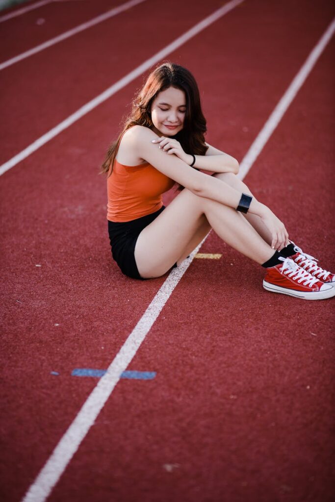 A young woman in athletic wear sits on a running track at a stadium, enjoying a moment of rest.