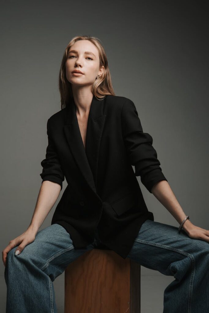 Fashion model in black blazer and jeans poses elegantly in a studio setting, showcasing modern style.