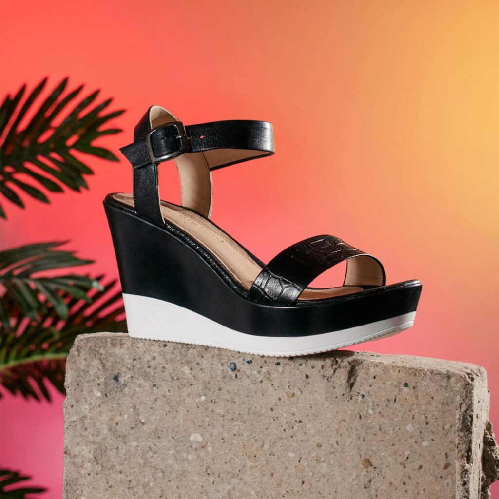 Black wedge sandal on a concrete block with a vibrant gradient background.