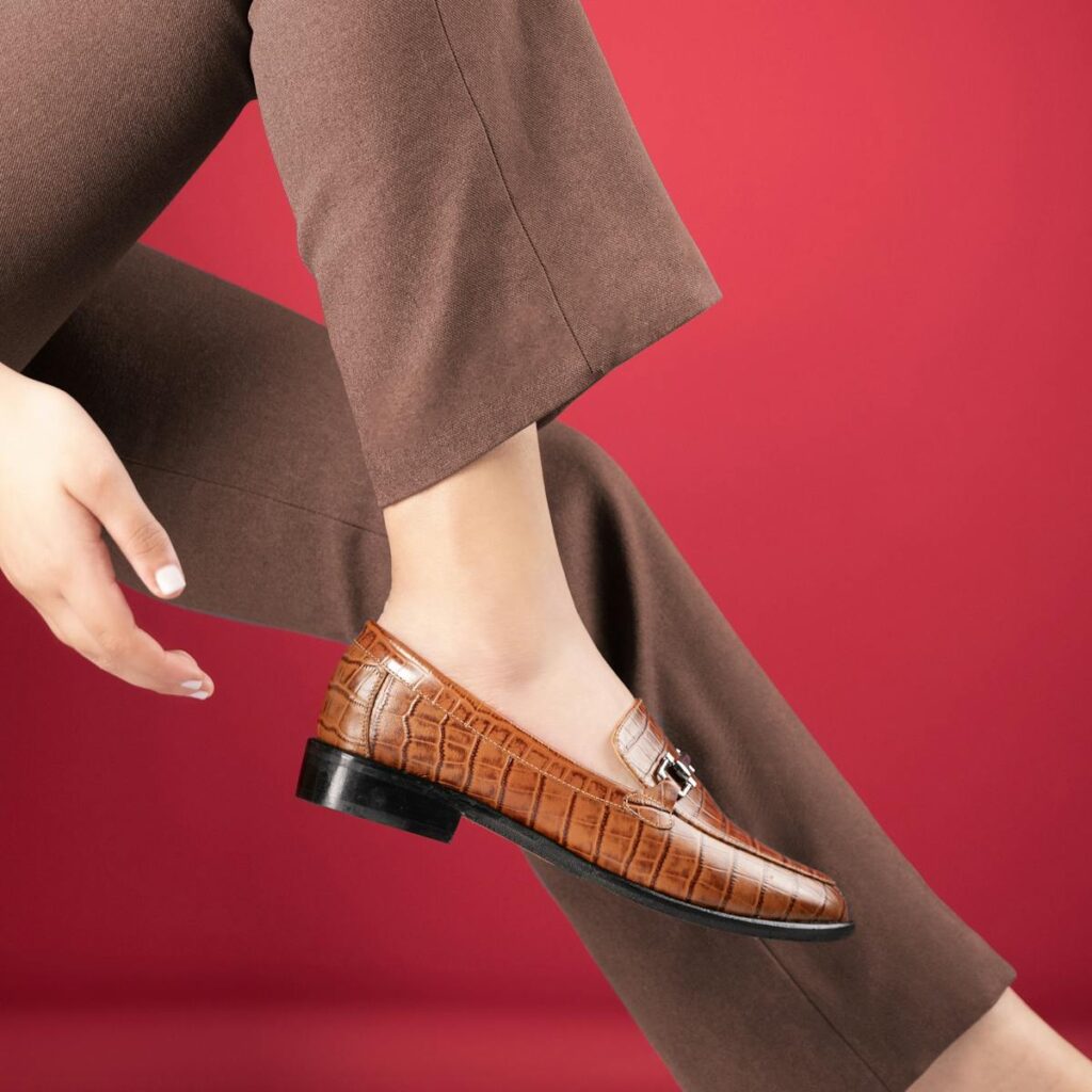 Fashionable brown leather loafer with buckle detail against a vibrant red backdrop.