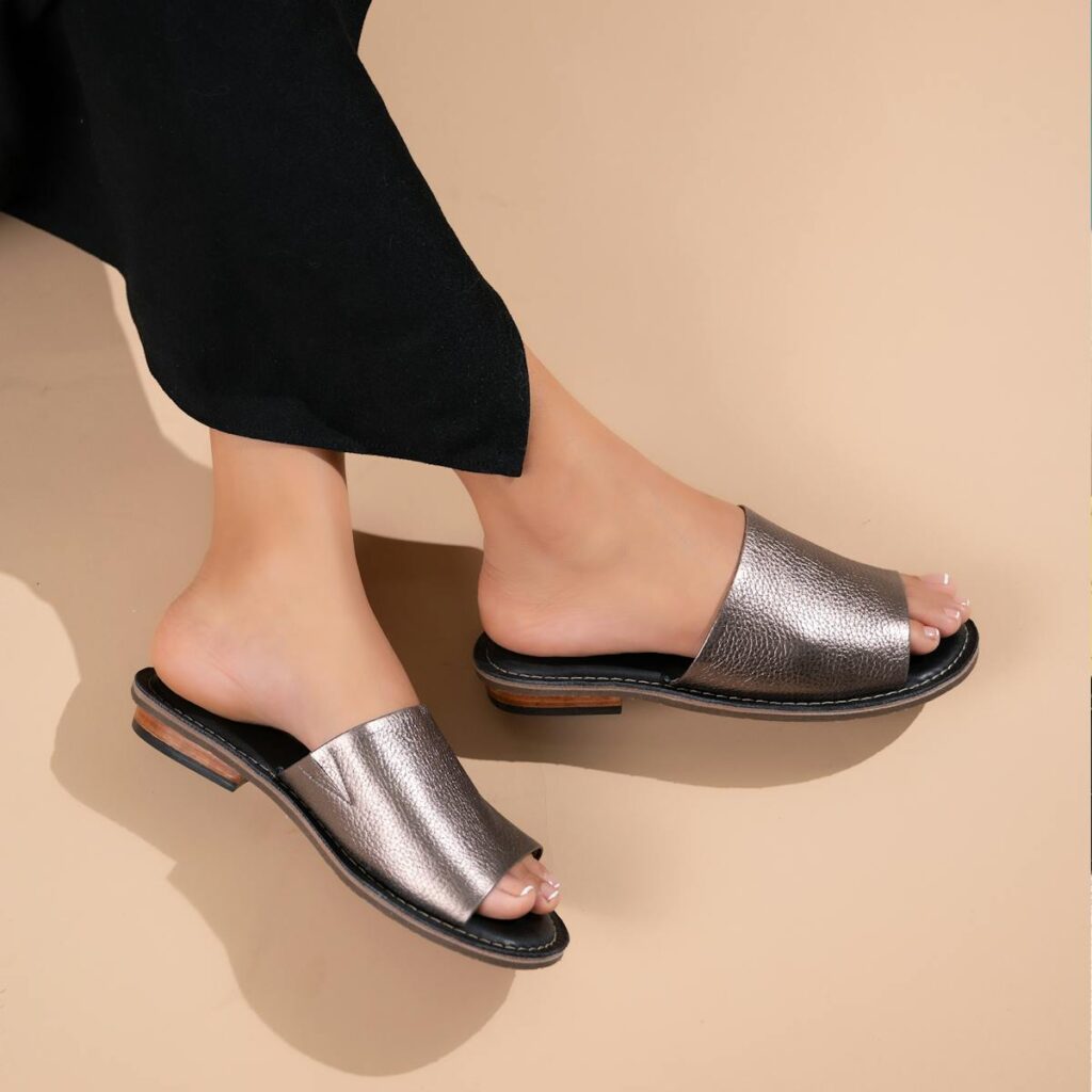 Stylish metallic slide sandals shown on a neutral beige background, highlighting modern footwear design.