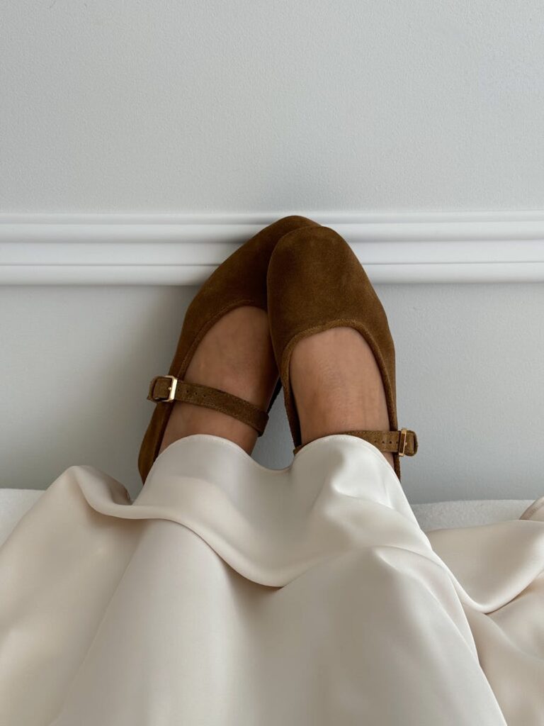 Brown suede shoes resting on white satin fabric indoors.