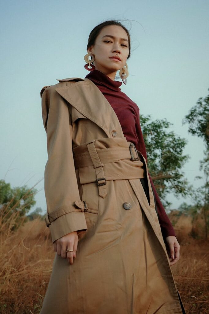 Fashionable woman in a trench coat posing confidently in a natural outdoor setting.