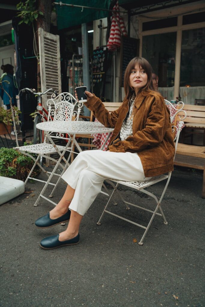 Woman in cozy autumn outfit sitting outdoors, holding a smartphone at a cafe.