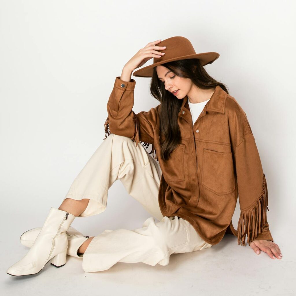 A stylish woman in a bohemian outfit poses against a minimalist background, showcasing modern fashion.
