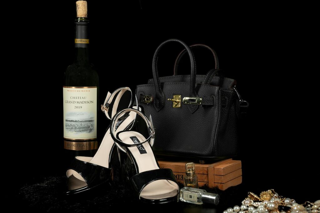 Luxury black handbag, shoes, and wine bottle paired with elegant jewelry create a sophisticated still life.