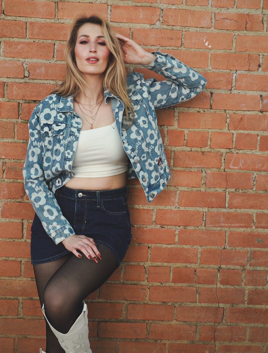 Fashionable young woman in denim jacket posing confidently outdoors.