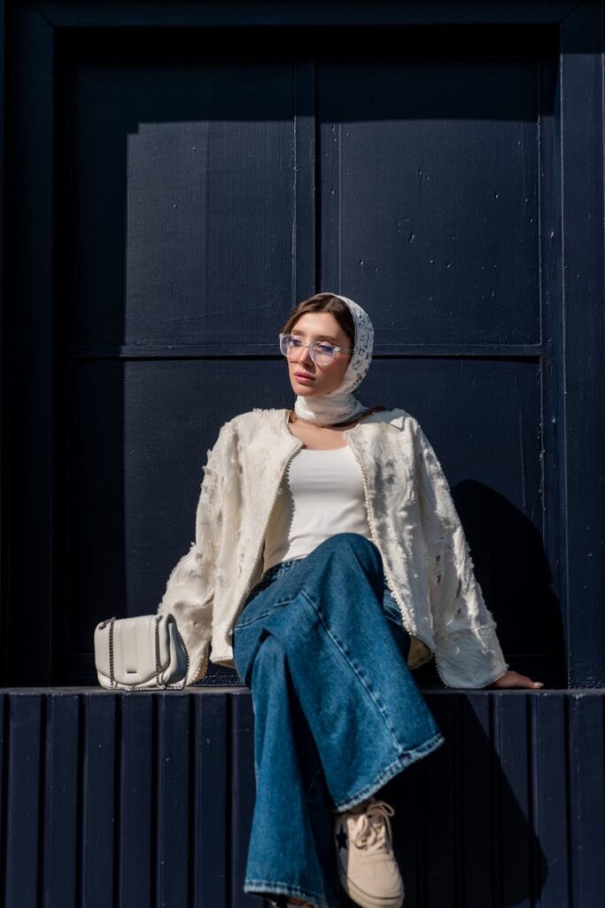 Fashionable woman in denim jeans and scarf posing against dark urban backdrop.
