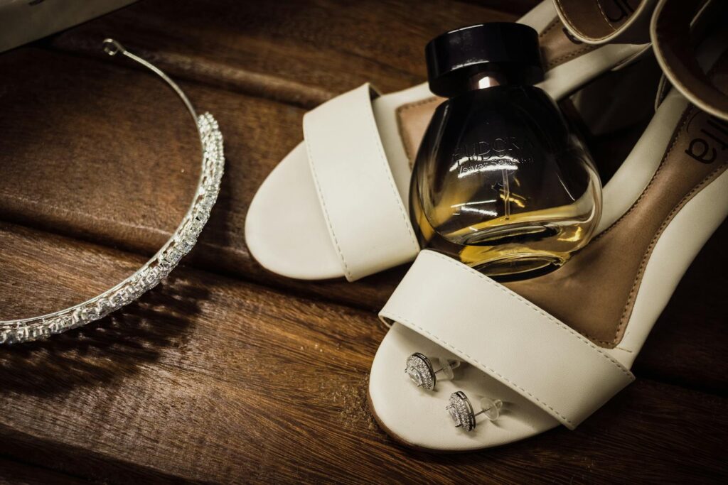 A stylish arrangement of bridal accessories including shoes, perfume, earrings, and a sparkling tiara on a wooden surface.