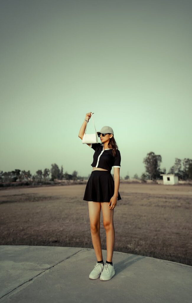 Stylish woman in black outfit posing on a sunny day outdoors with green hues.
