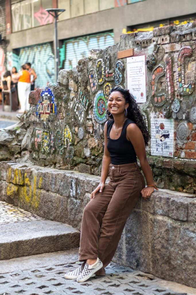 Happy woman sitting on stone bench by decorative mosaic wall in urban setting.