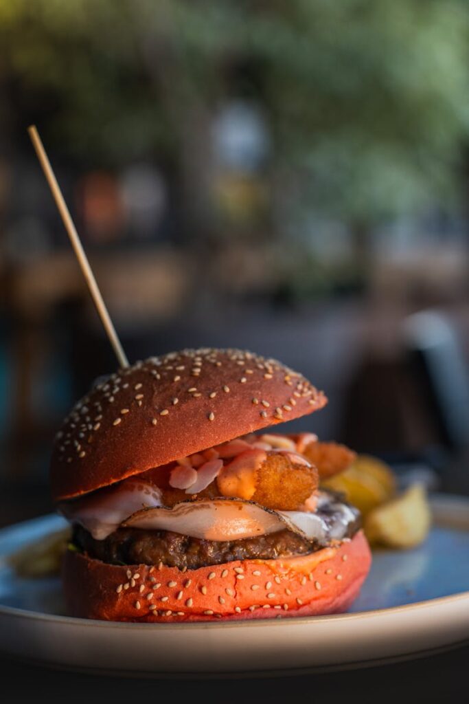 Delicious gourmet hamburger with a vibrant red bun, cheese, and potatoes on a plate.