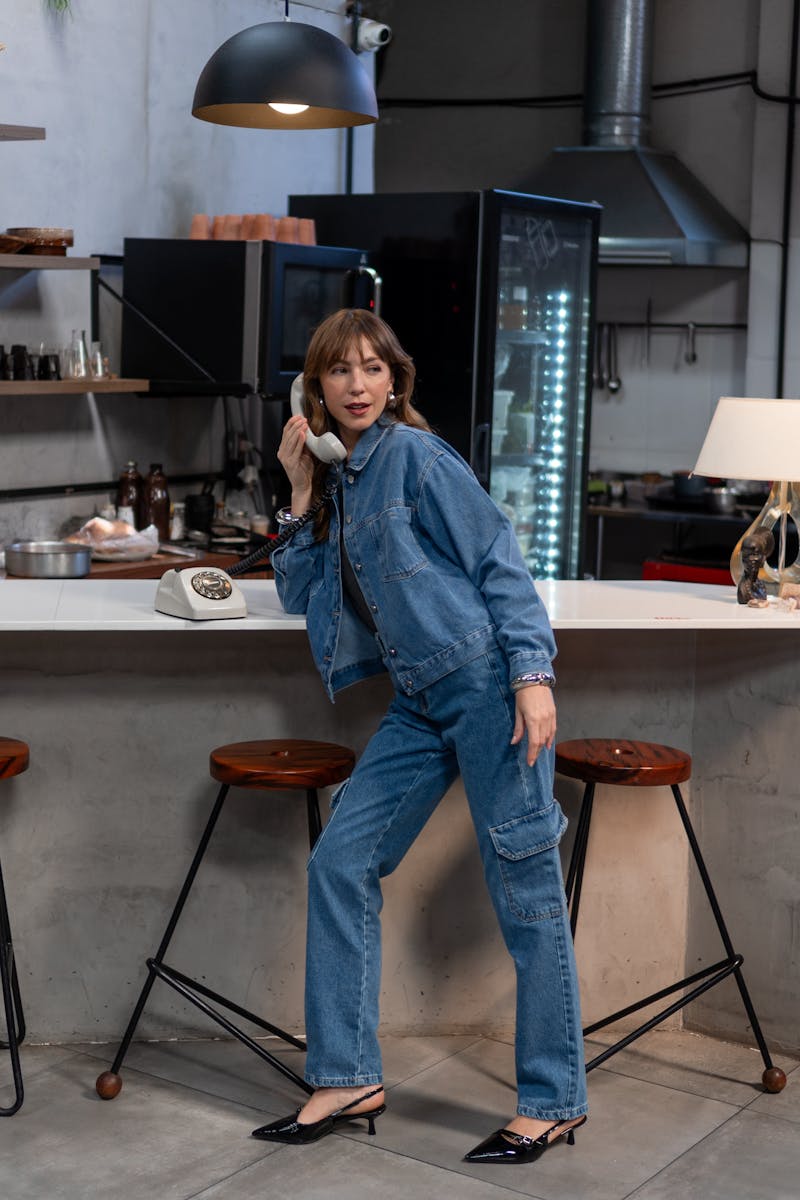 Stylish woman in denim speaks on vintage rotary phone in a contemporary kitchen setting.
