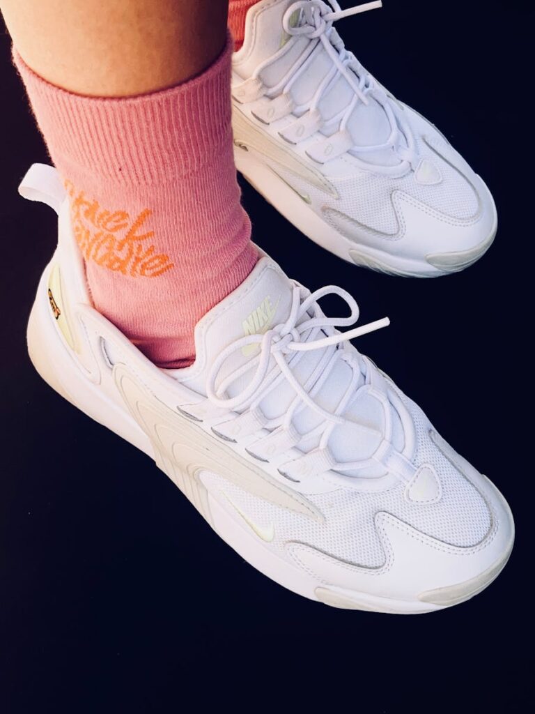 Close-up view of white sneakers paired with pink text socks against a dark backdrop.
