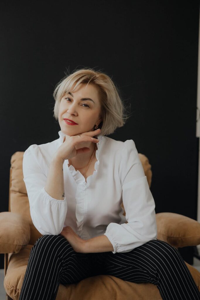 Stylish woman in white blouse and striped pants sitting confidently on a chair.