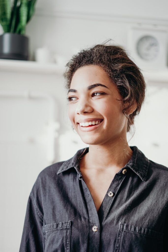A cheerful woman smiling indoors, dressed in casual attire, evoking a sense of happiness and relaxation.
