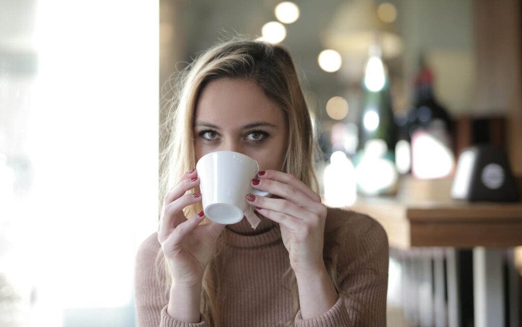 A young woman in a cozy sweater sipping a hot beverage in a relaxed indoor setting.