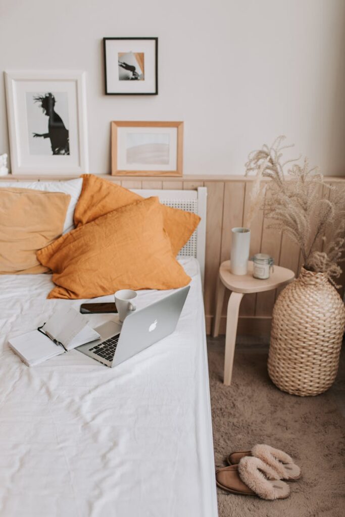 A stylish bedroom setup featuring a laptop, orange pillows, and modern decor.
