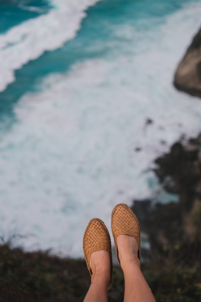 Pair of woven shoes over a cliff with ocean waves below, symbolizing travel freedom.