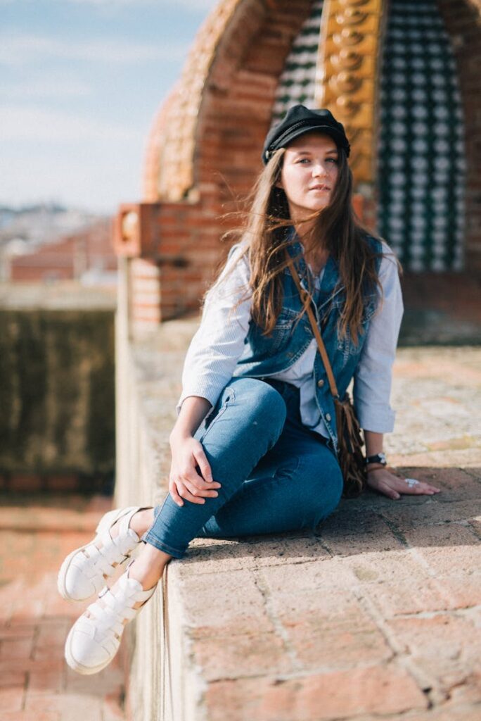 Fashionable young woman sitting on a brick wall wearing casual style with a beret outdoors.
