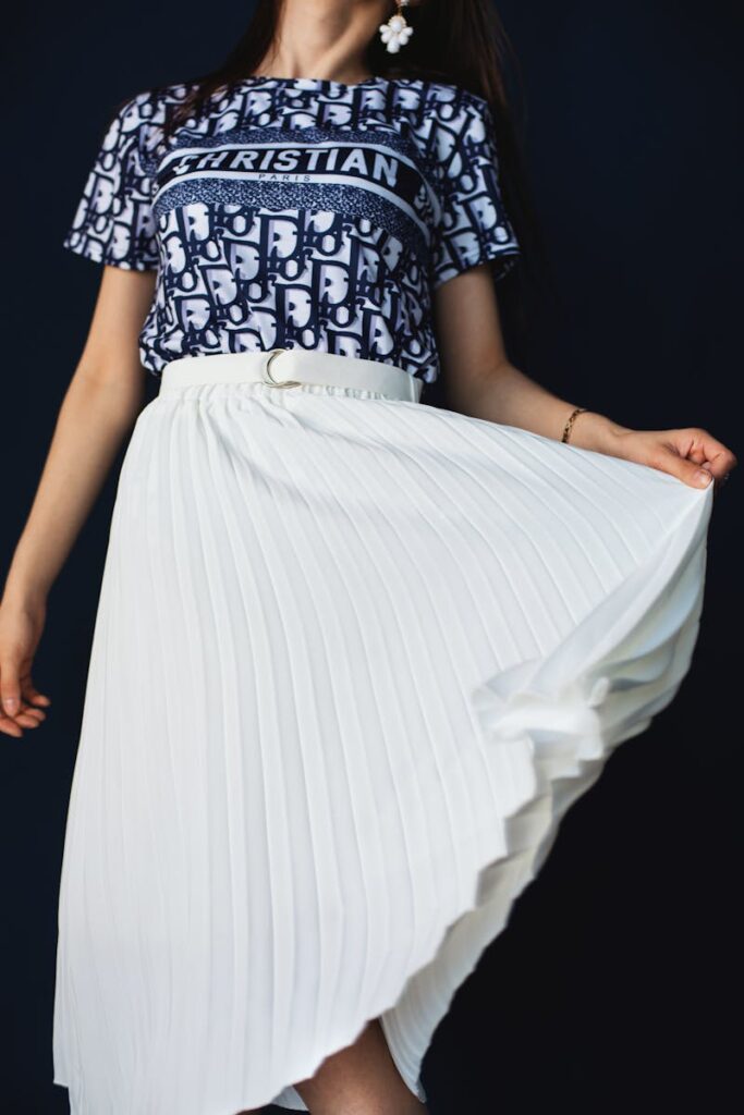 Fashionable woman posing in a studio with a printed blouse and pleated white skirt.