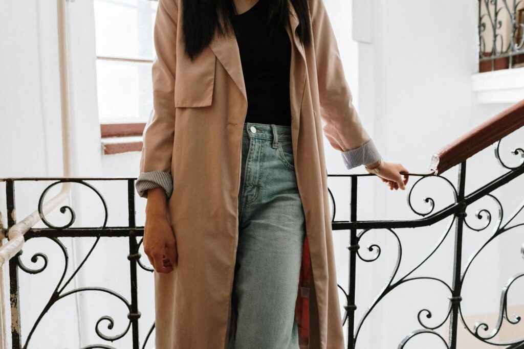 A fashionable woman in jeans and a coat stands on a vintage staircase with wrought iron railings.