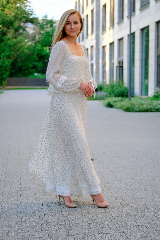 Full body of adult elegant female in maxi stylish dress standing on paved street and looking at camera
