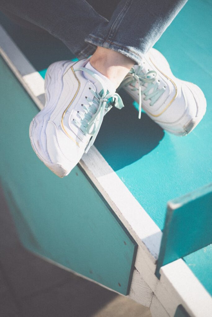 Close-up of trendy white sneakers resting on a vibrant turquoise surface with sunlight.