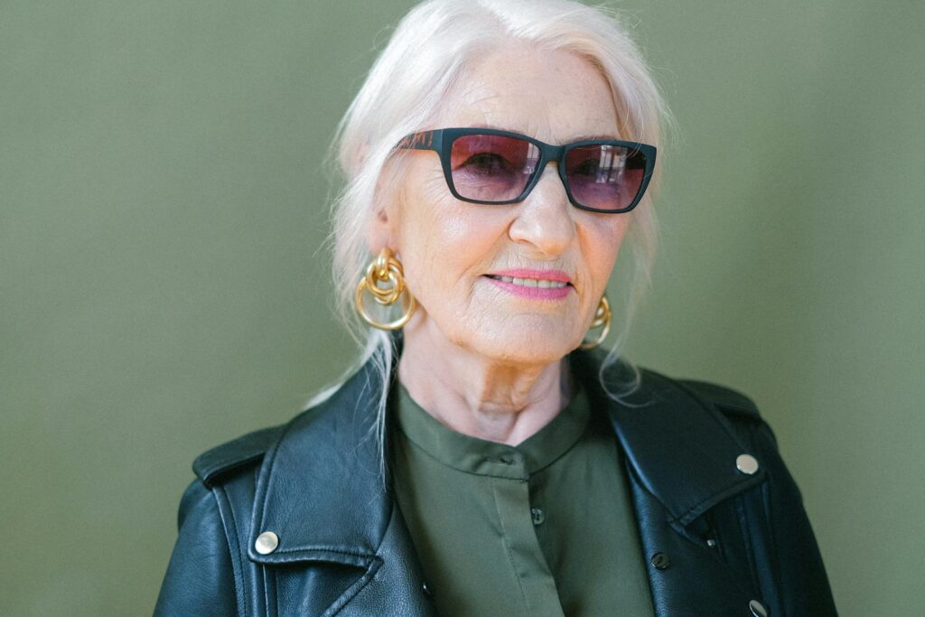 Crop aged confident female in stylish leather jacket and sunglasses looking at camera on green background of studio