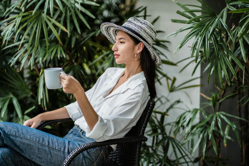 Young woman enjoys a hot drink on a lush terrace, embodying relaxation and style.