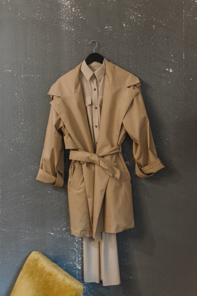 Stylish beige trench coat hanging on a black hanger against a rustic gray wall with texture.