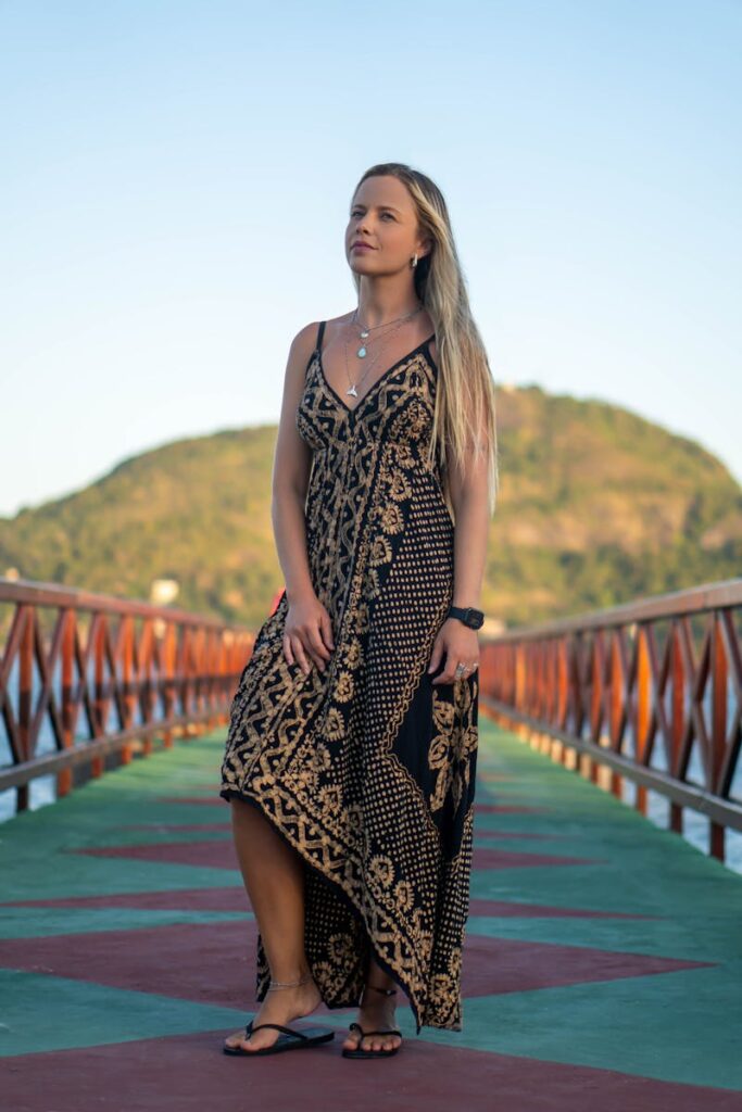A woman in an elegant dress poses gracefully on a picturesque wooden bridge.