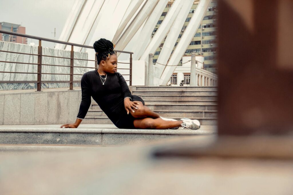 Trendy ethnic female in elegant apparel with hairdo looking away while sitting on staircase on street