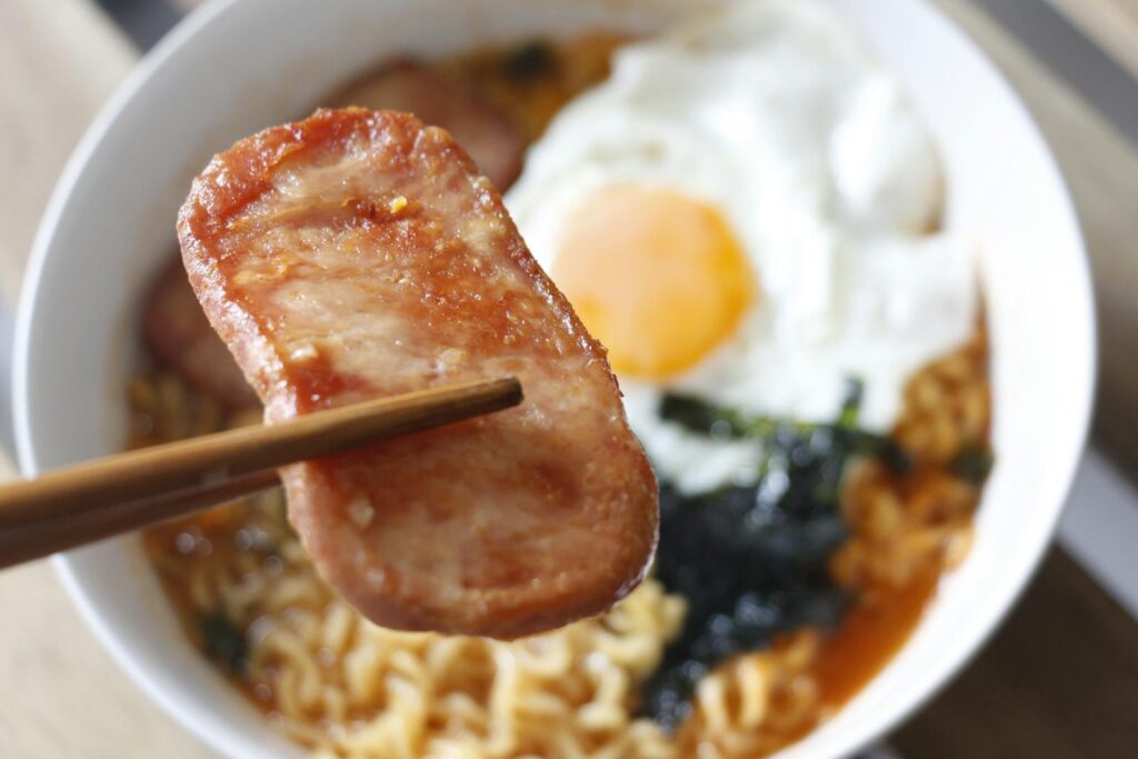 Close-up of a tasty noodle bowl with fried egg and Spam, perfect Asian cuisine delight.