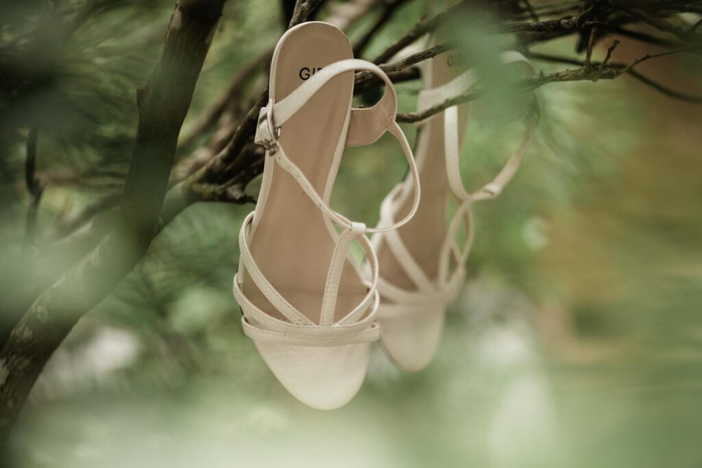 Beige strappy sandals elegantly hanging on branches in a lush outdoor setting.
