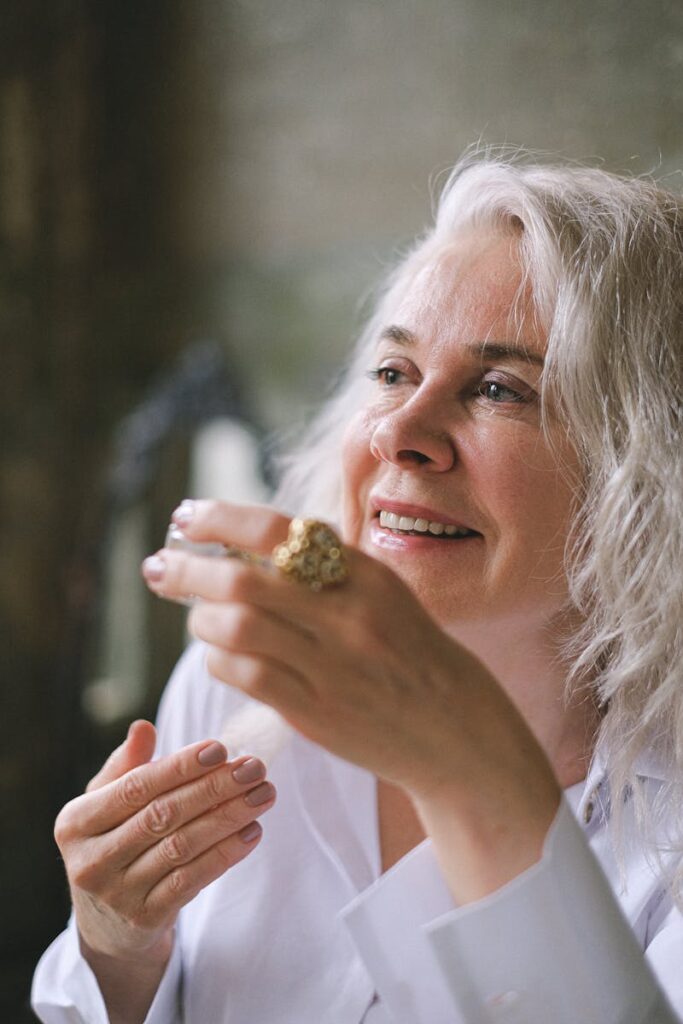 A senior woman with white hair holds a coffee cup, smiling thoughtfully indoors.