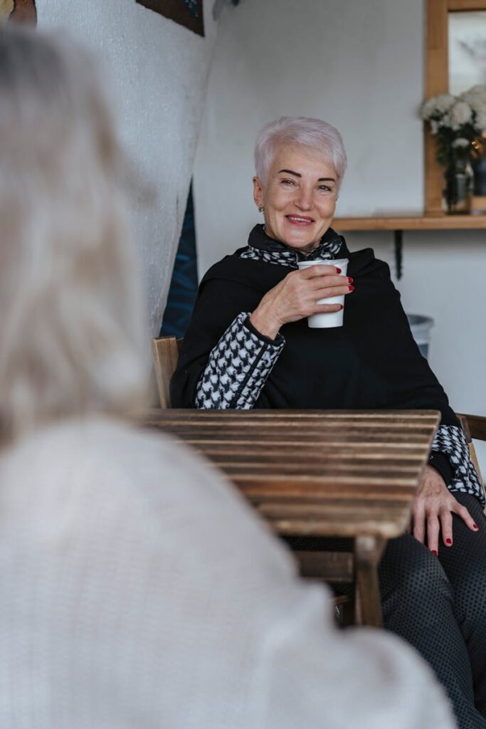 Senior woman with short hair smiling while holding a cup of coffee at a cozy indoor cafe.