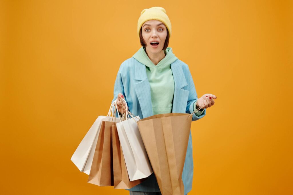 A woman in vibrant clothes holds several shopping bags against a solid background.