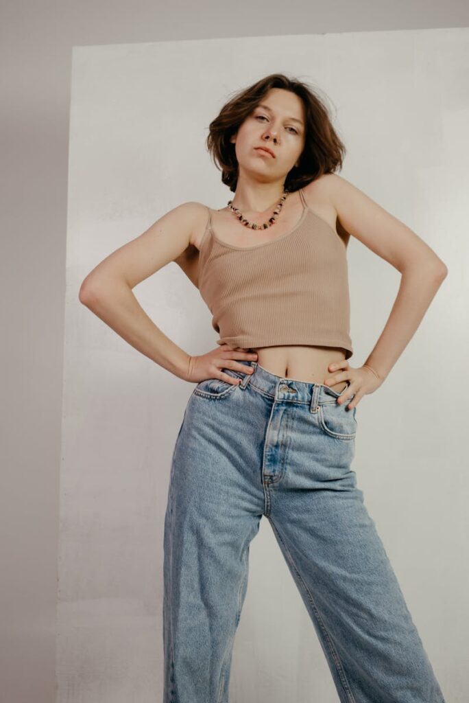 Young woman in casual fashion posing confidently indoors wearing a tank top and jeans.