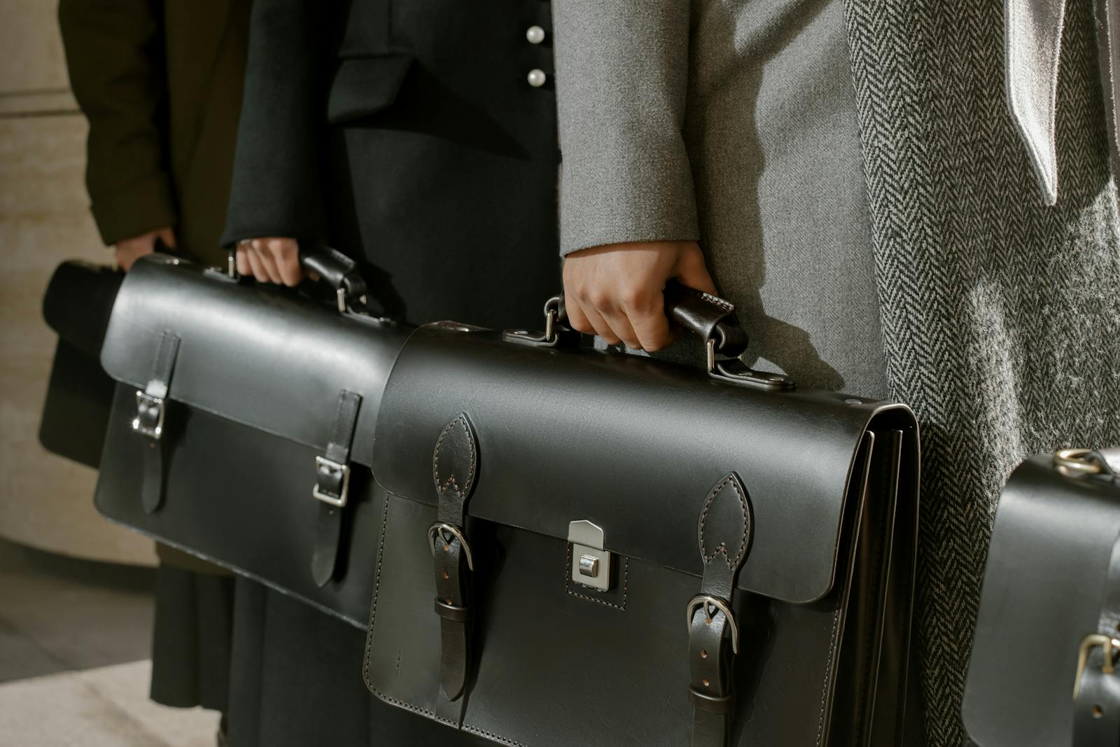 Group of adults holding sleek leather briefcases in formal business attire, emphasizing corporate professionalism.