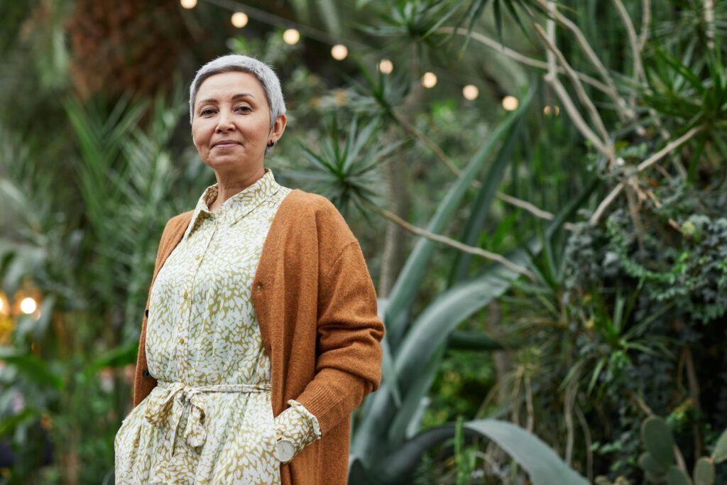 Senior woman in a stylish outfit enjoying a peaceful garden setting.