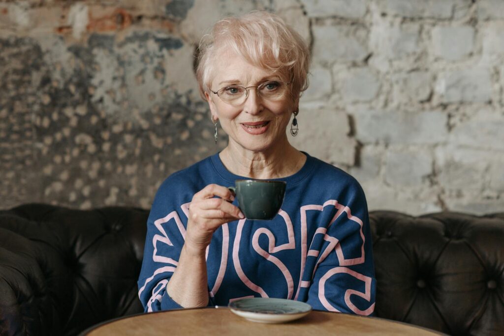 Senior woman with glasses enjoying a cup of coffee in a cozy cafe setting. Relaxed and content atmosphere.