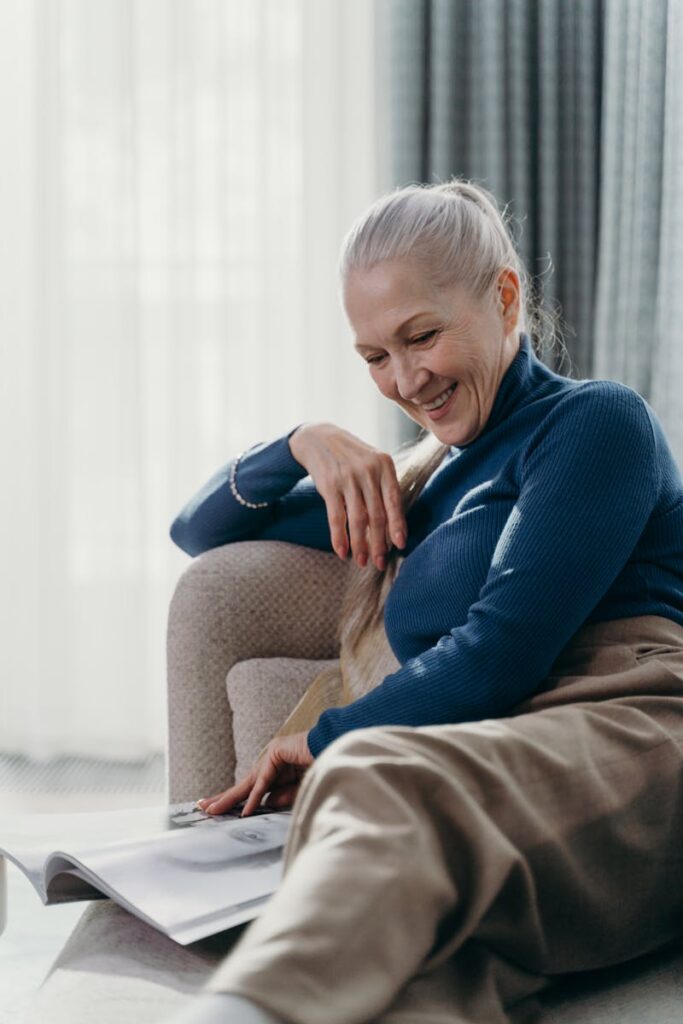 Elderly woman enjoying a quiet moment at home, reading a magazine with a smile.