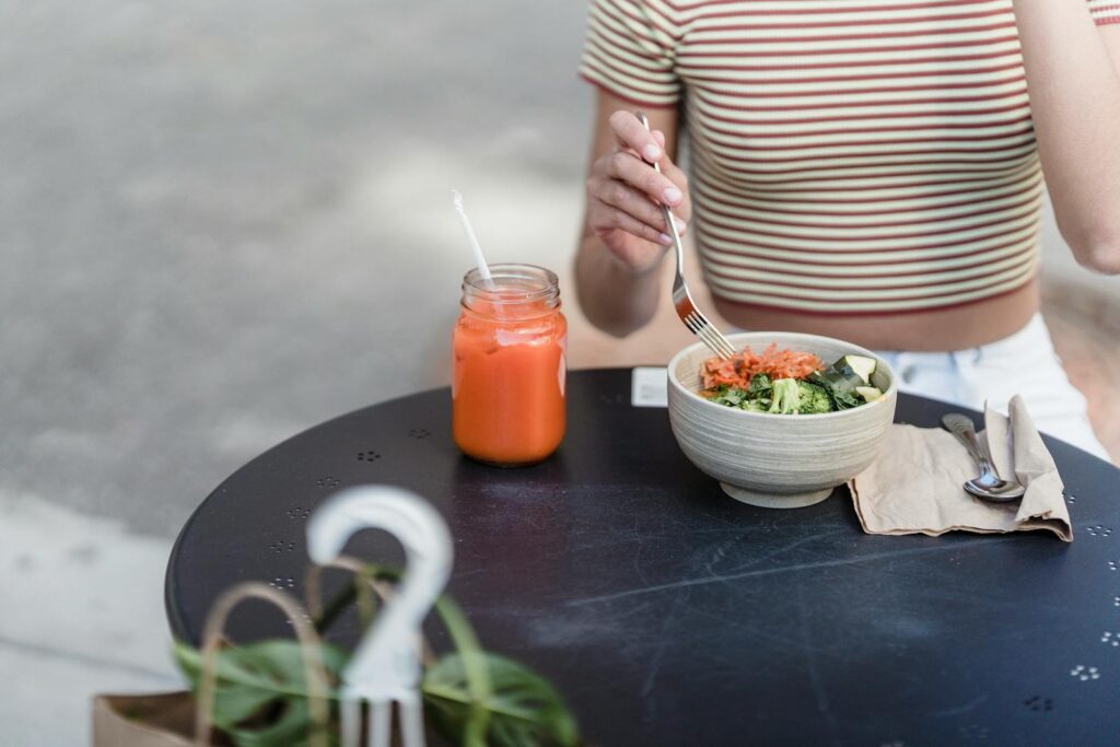 Woman enjoying a fresh salad and juice outdoors, promoting healthy lifestyle.