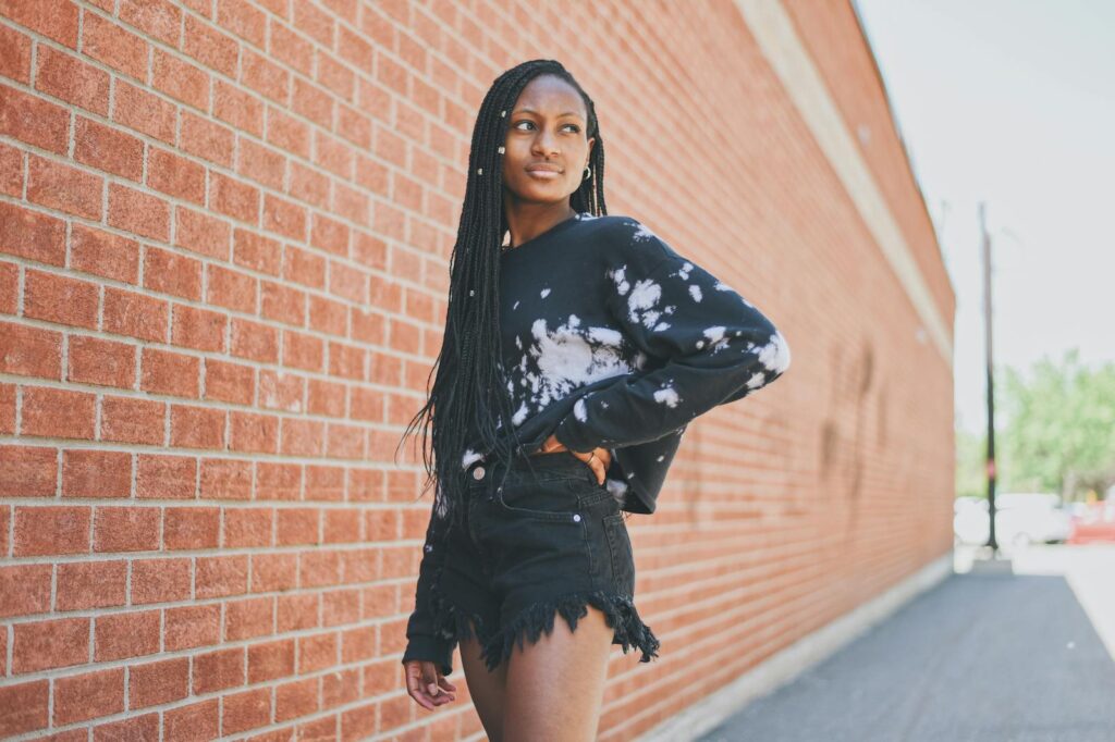 Confident young woman in casual attire by a brick wall, exuding urban style and attitude.