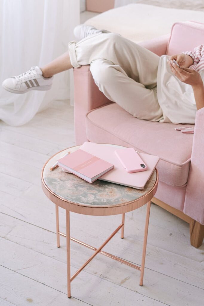 Person relaxing on pink sofa with notebook and smartphone, perfect for lifestyle themes.